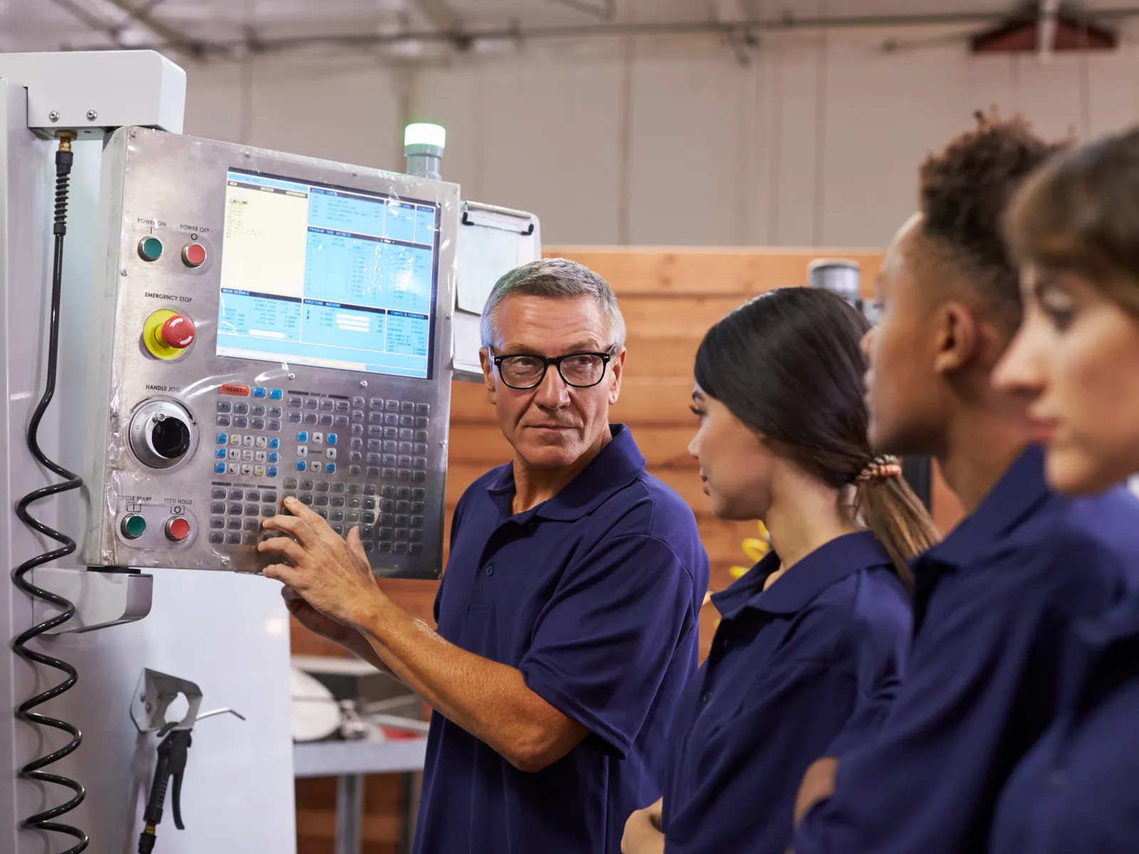 Ausbilder erklärt Lehrlingen die Steuerung einer CNC-Maschine